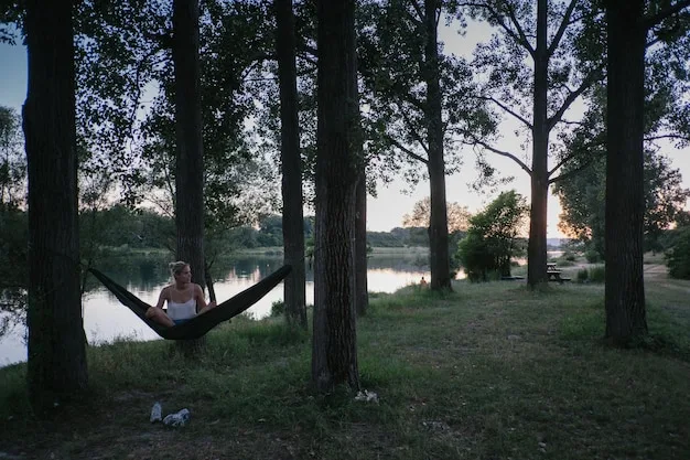 A person relaxing in a hammock strung between two trees in a peaceful forest setting. Sunlight filters through the leaves, creating a dappled effect. The person is holding a book and appears to be fully immersed in reading and relaxation.