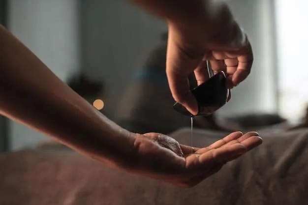 A close-up shot of a hand carefully pouring a few drops of essential oil from a small amber bottle into a tablespoon of carrier oil (almond or jojoba oil). The background is softly blurred, with a bathtub partially visible.