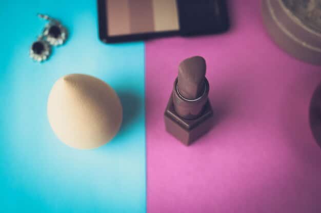 A well-lit close-up of various makeup products arranged neatly on a vanity, including foundation, concealer, eyeshadows in neutral and dark shades, mascara, eyeliner, lipstick in both nude and bold colors, blush, and highlighter. Brushes of different sizes and shapes are also visible.