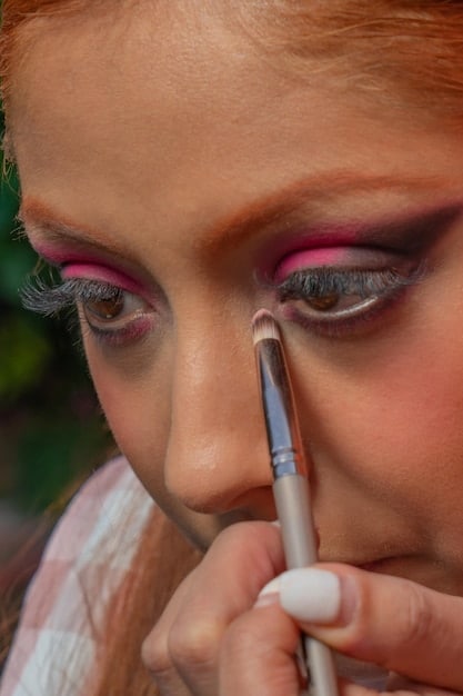 A detailed close-up of a makeup artist using a small, precise brush to apply concealer to the eyelid, creating the sharp line of the cut crease.