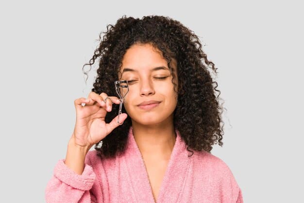 A person holding a strip of false lashes up to their eye to measure the length. They are using small scissors to carefully trim the outer edge of the lash strip.