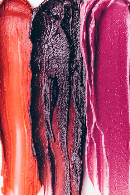 A close-up of several lipsticks and lip tints in different shades, ranging from deep reds and berry tones to soft pinks and nudes. The arrangement is on a clean white surface, highlighting the textures and colors of the products.