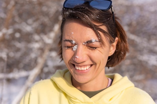 A young woman applying sunscreen to her face while outdoors on a sunny winter day. She is smiling and wearing a winter hat.