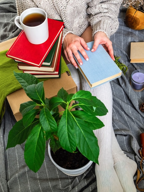 A person sitting comfortably in an armchair, holding a journal and a pen, with a cup of tea on a nearby table. The room is warmly lit and decorated with plants, creating a serene atmosphere.
