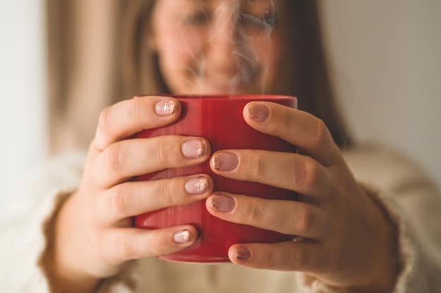 A close-up shot of a person's hands gently holding a steaming cup of herbal tea on a sunny morning. In the background, a garden can be seen slightly blurred, suggesting a peaceful and natural environment.