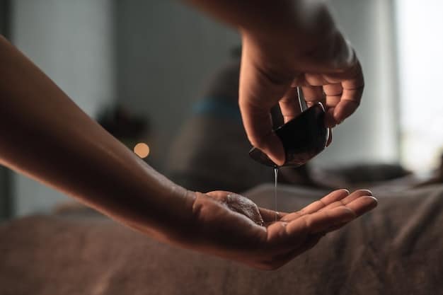 A close-up shot of a hand carefully pouring a few drops of essential oil from a small amber bottle into a tablespoon of carrier oil (almond or jojoba oil). The background is softly blurred, with a bathtub partially visible.